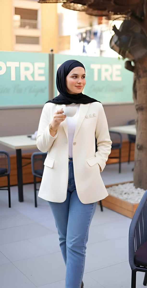 ZAYTA Off-white tailored blazer on model wearing black hijab, showing fabric and inner lining, standing outdoors with blurred background