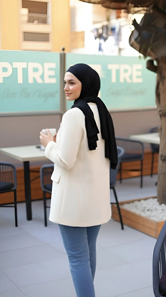 ZAYTA tailored blazer on model wearing hijab, showing fabric and inner lining, holding a coffee cup in outdoor cafe setting
