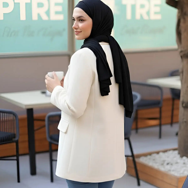 ZAYTA tailored blazer on model wearing hijab, showing fabric and inner lining, holding a coffee cup in outdoor cafe setting