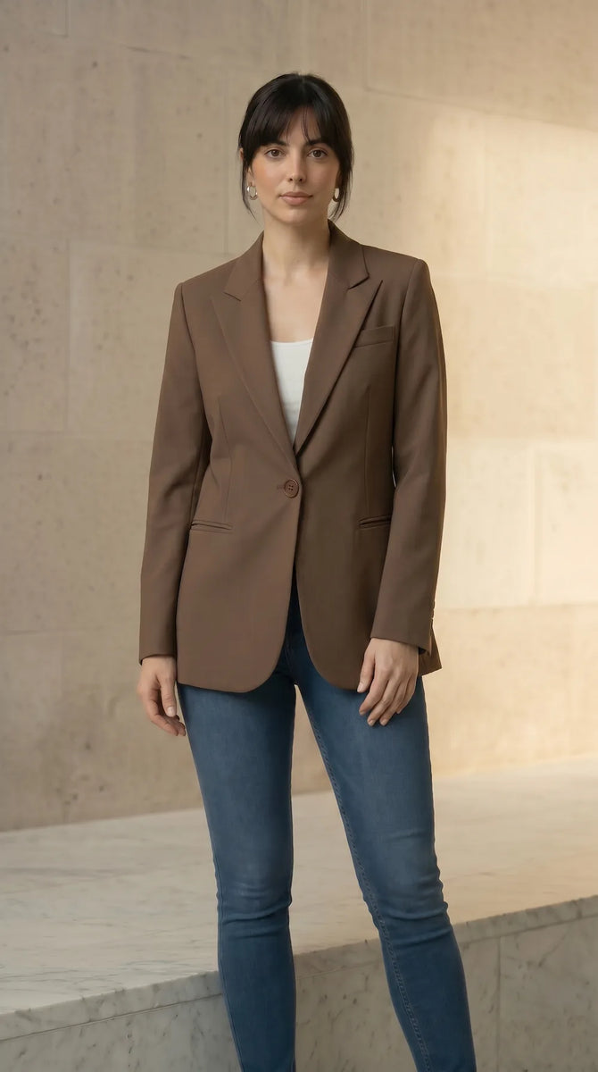 Woman wearing a mocha blazer and blue jeans against a neutral background