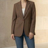 Woman wearing a mocha blazer and blue jeans against a neutral background