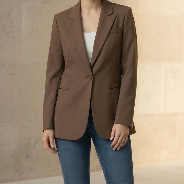 Woman wearing a mocha blazer and blue jeans against a neutral background