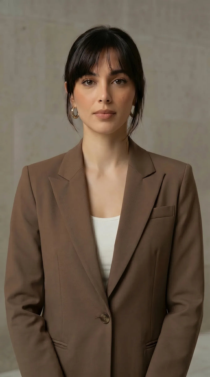 Woman wearing a mocha blazer over a white top against a neutral background