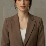 Woman wearing a mocha blazer over a white top against a neutral background