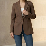 Woman wearing a mocha blazer and blue jeans with a beige handbag on a neutral background